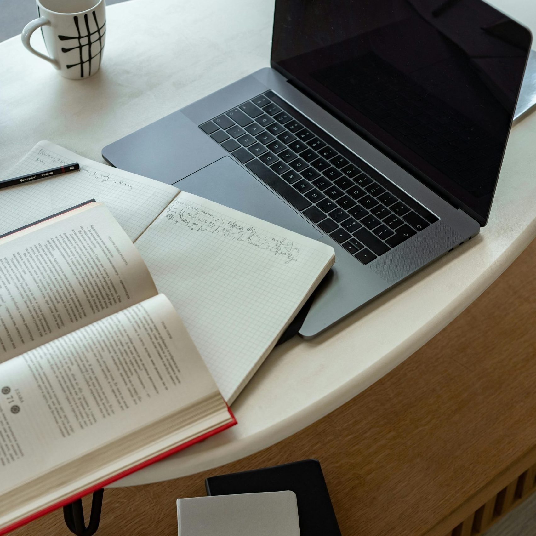 A cozy indoor workspace featuring a laptop, open book, notepad, and coffee, perfect for studying or remote work.